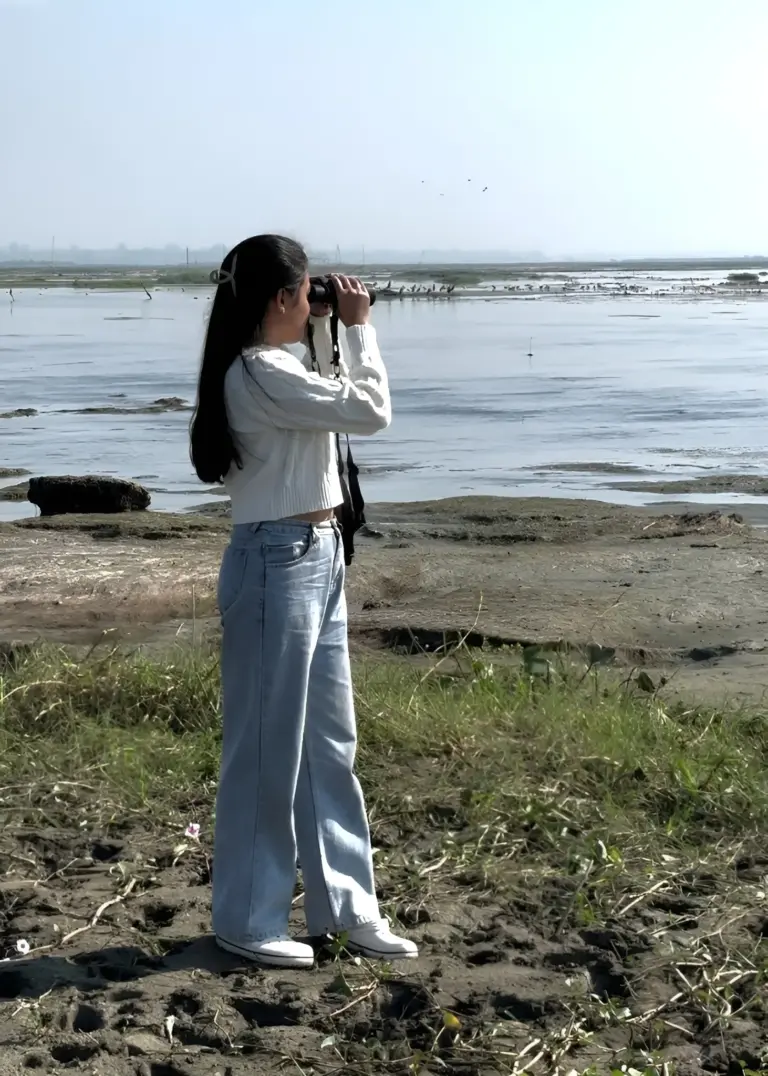 A girl birdwatching with binoculars by the wetlands at Maguri Beel, Assam