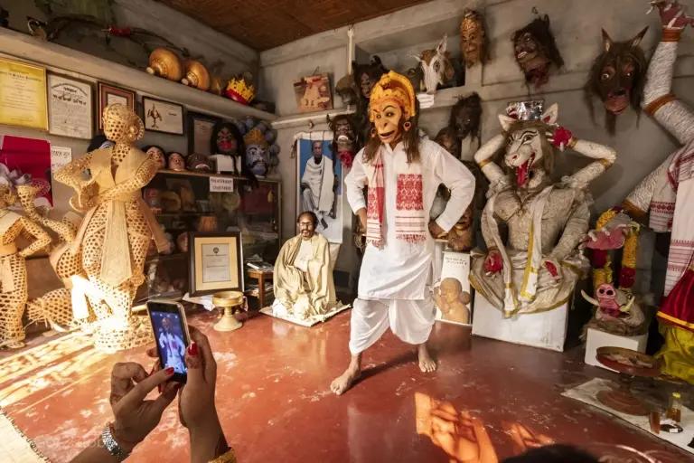 A visitor photographs a masked performer inside Samuguri Satra, Assam
