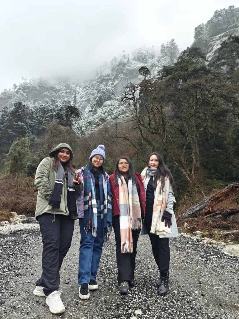 Four women posing on a rocky path with snow-covered mountains in Anini, Arunachal Pradesh