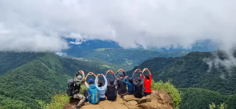 Group of friends sitting on a cliff making heart shapes with hands at Dzukou Valley