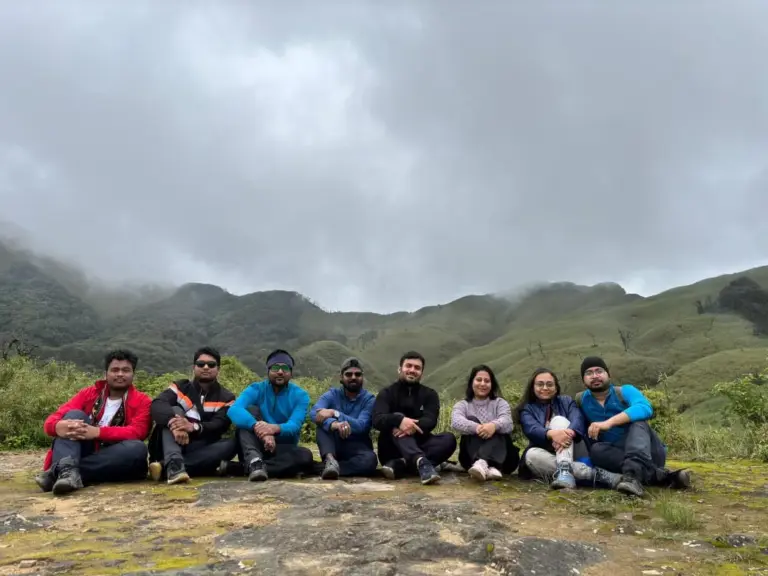 Group of friends sitting together with misty green hills in the background at Dzukou Valley