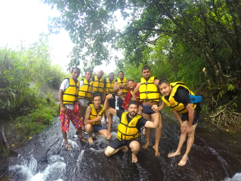 Group of people wearing life jackets posing on a rocky stream at Mawlyngbna, Meghalaya