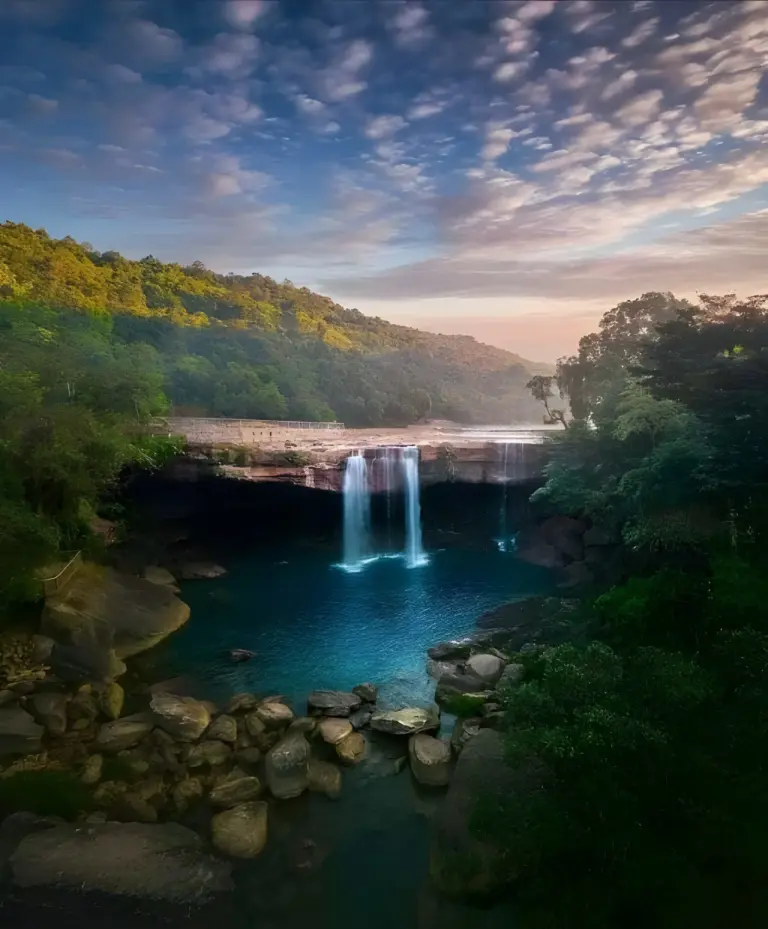 Karng Suri Falls in Meghalaya with waterfalls flowing into a deep blue pool surrounded by forest and rocks
