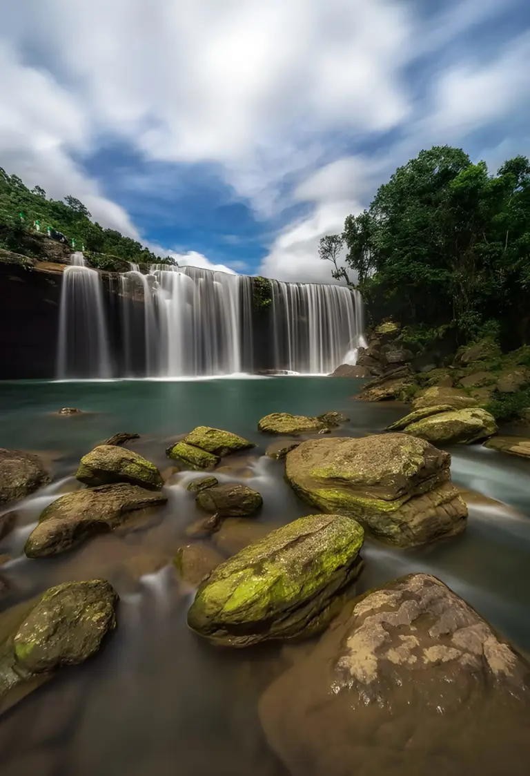 Krang Suri Falls in Meghalaya, with water cascading into a clear blue pool surrounded by rocks and greenery