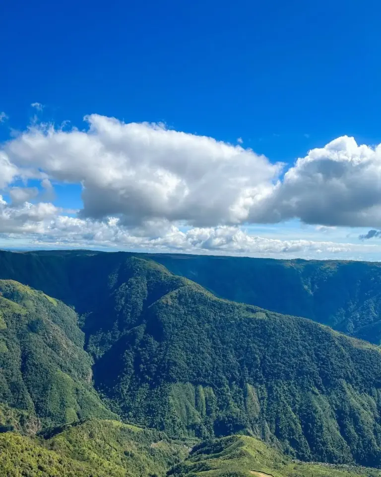 Lush green hills under a bright blue sky with scattered clouds in Laitlum, Meghalaya