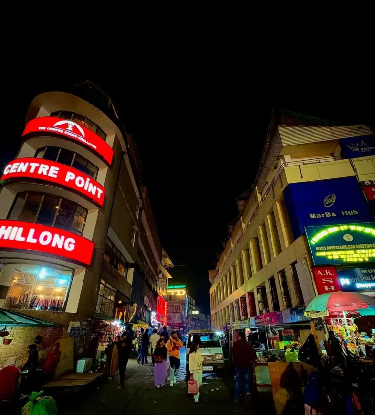 Night street scene at Police Bazar, Shillong, with shoppers, street vendors, and colorful building lights
