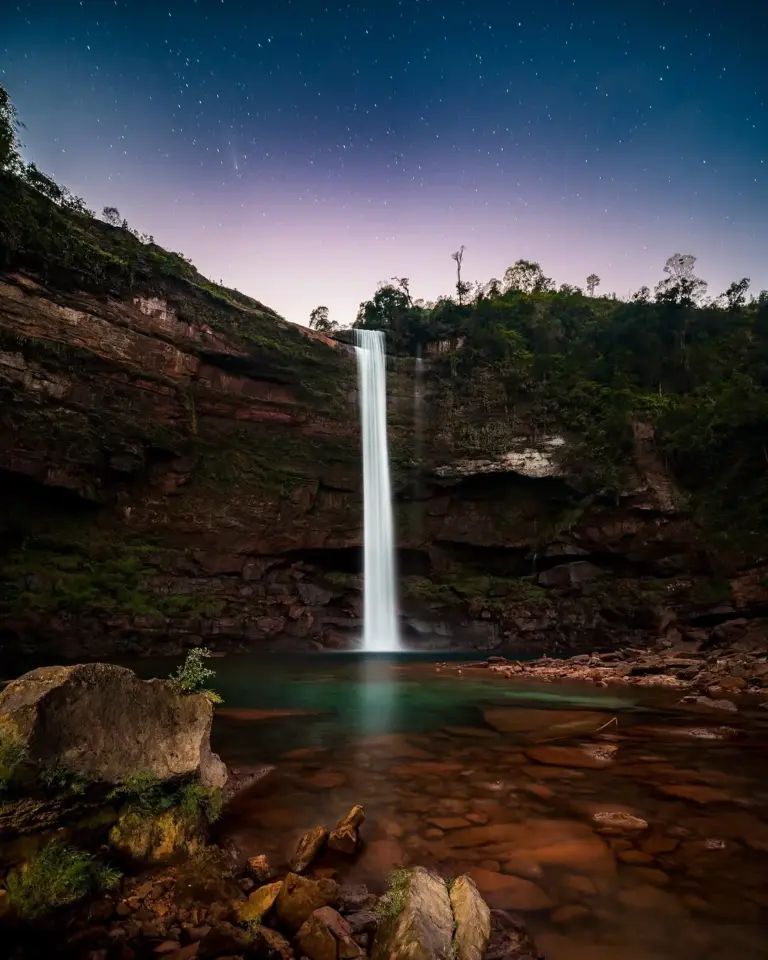 Night view of Phe Phe Falls cascading into a clear pool, surrounded by cliffs in Meghalaya