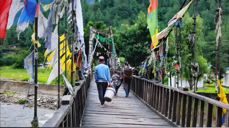 People walking across a prayer flag-decorated wooden bridge at Sangti Valley