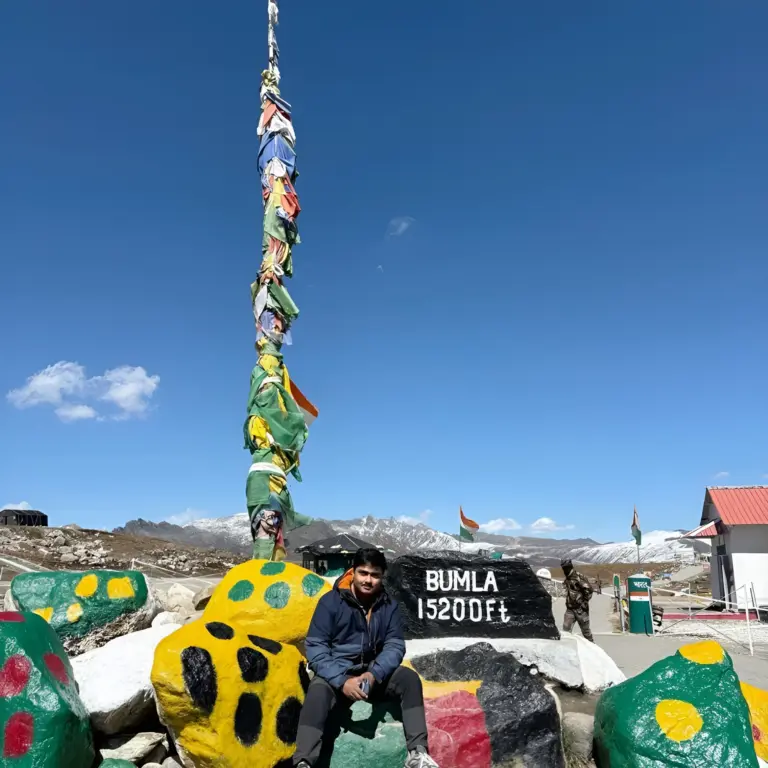 Person sitting near Bumla Pass sign at 15,200 ft in Arunachal Pradesh
