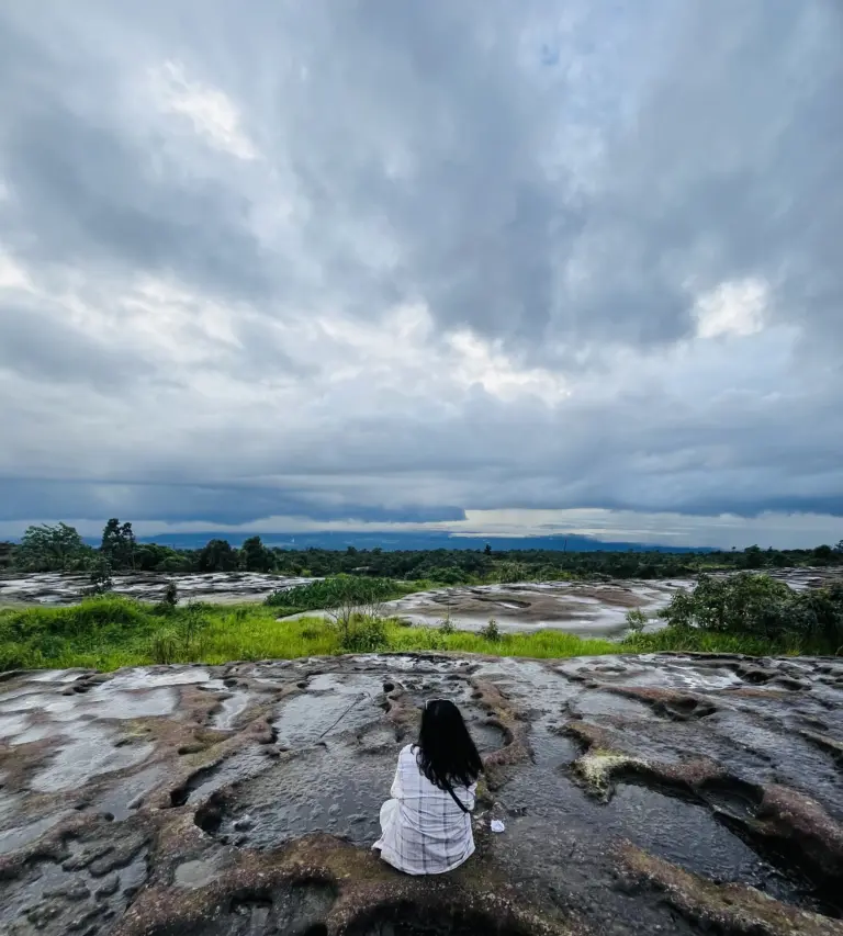 Person sitting on rocky terrain under a cloudy sky at Mawlyngbna Meghalaya