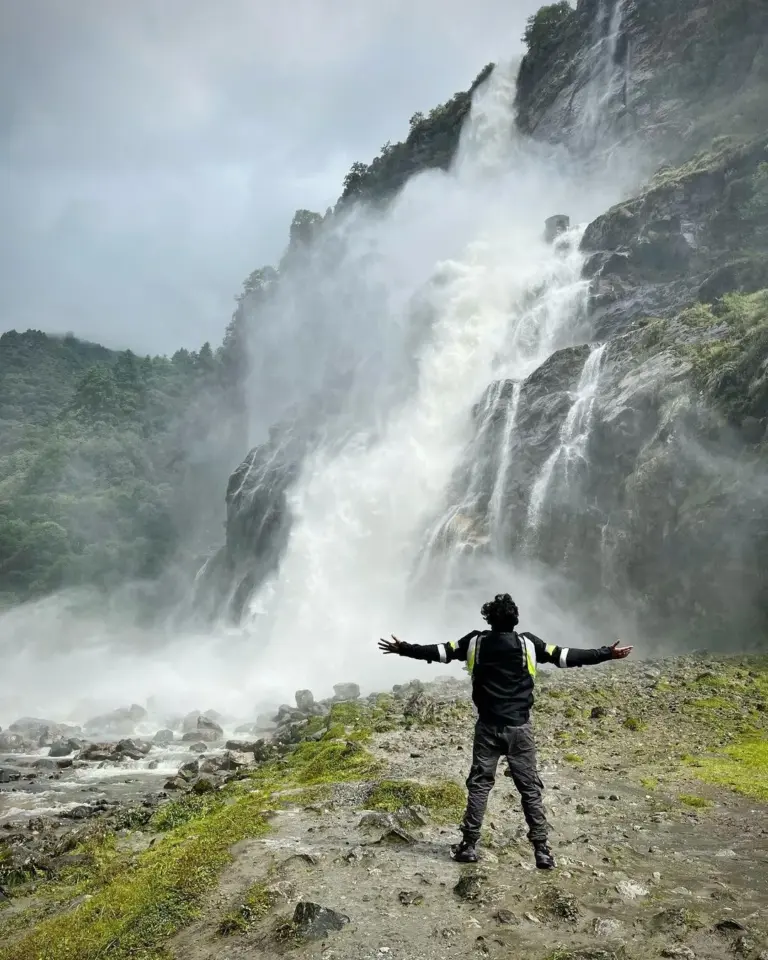Person standing with open arms in front of the powerful Nuranang Falls in Arunachal Pradesh