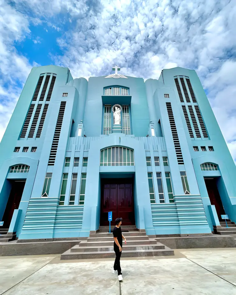 Person walking in front of the blue Shillong Cathedral under a dramatic cloudy sky