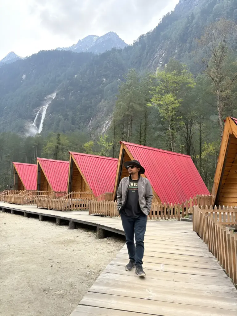 Person walking near cabins with mountains in Anini, Arunachal Pradesh