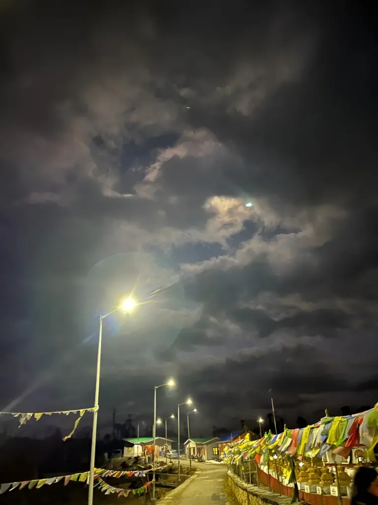 Prayer flags and streetlights under a dramatic night sky at Mandala Top