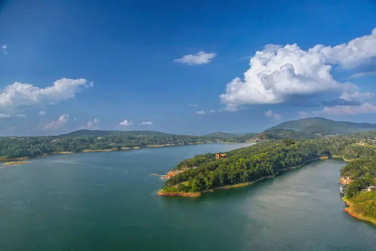 Scenic aerial view of Umiam Lake in Meghalaya, surrounded by lush green hills under a vibrant blue sky with scattered clouds