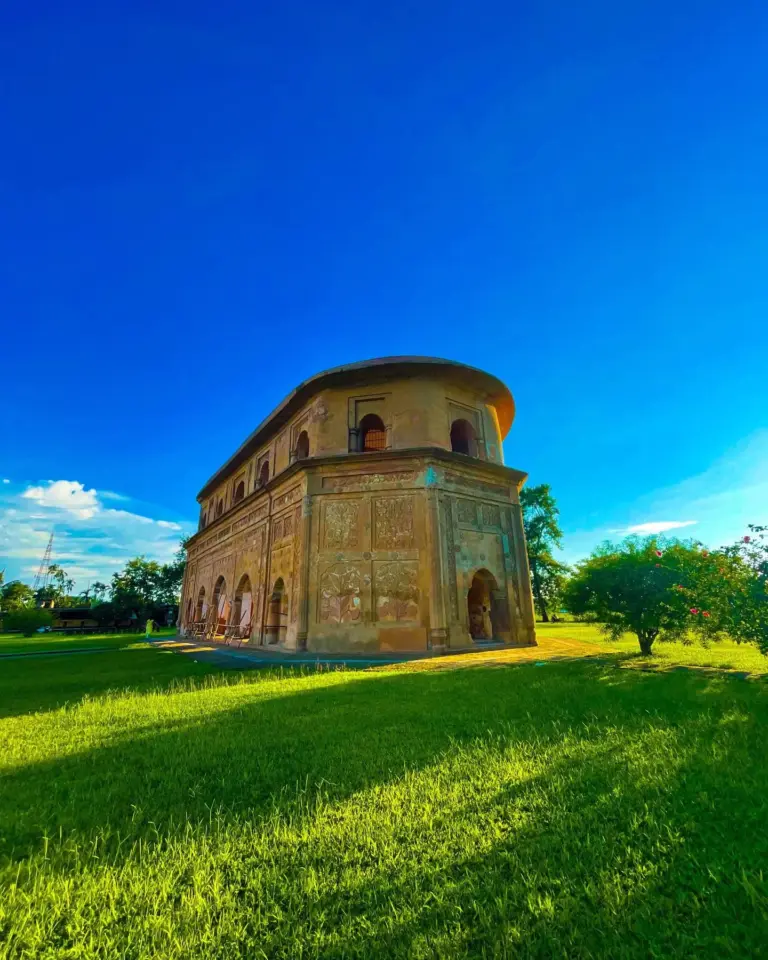 Side view of Rang Ghar in Assam, captured under a vibrant blue sky and lush green surroundings