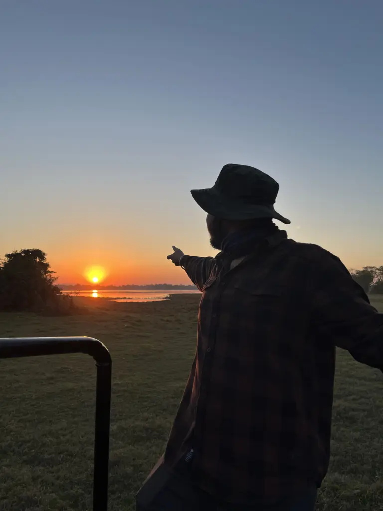 Silhouette of a guide pointing toward sunrise over wetlands in Pobitora