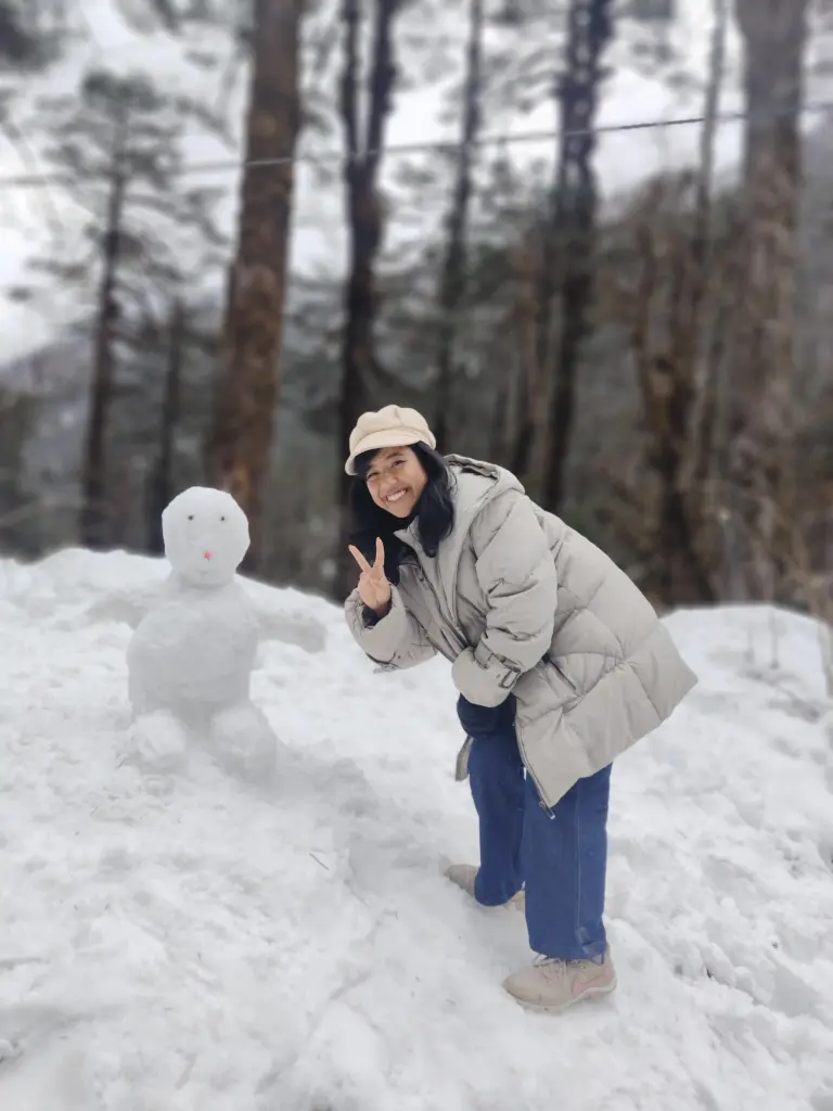 Smiling woman posing with a snowman in snowy Mechuka, Arunachal Pradesh