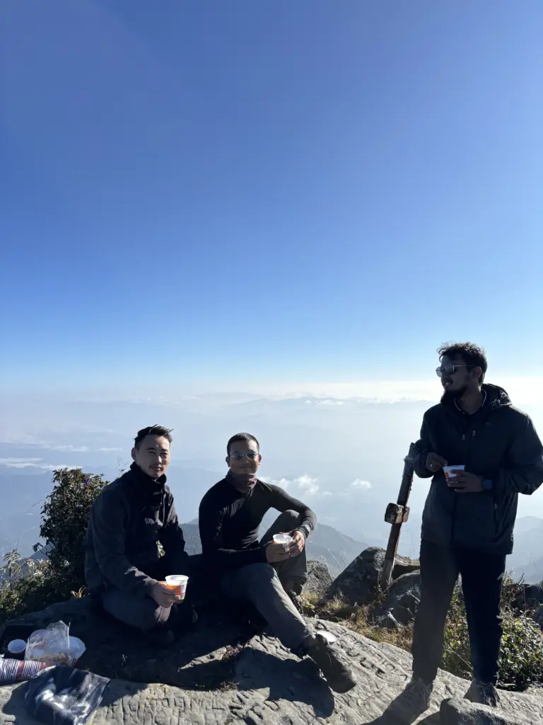 Three friends enjoying tea at the summit of Japfu Peak with mountain views