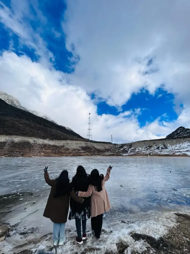 Three friends stand together facing a frozen Sela Lake in Arunachal Pradesh