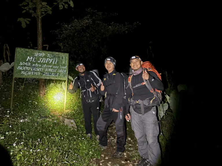 Three trekkers posing at the Mt Japfu trail signboard at night with headlamps