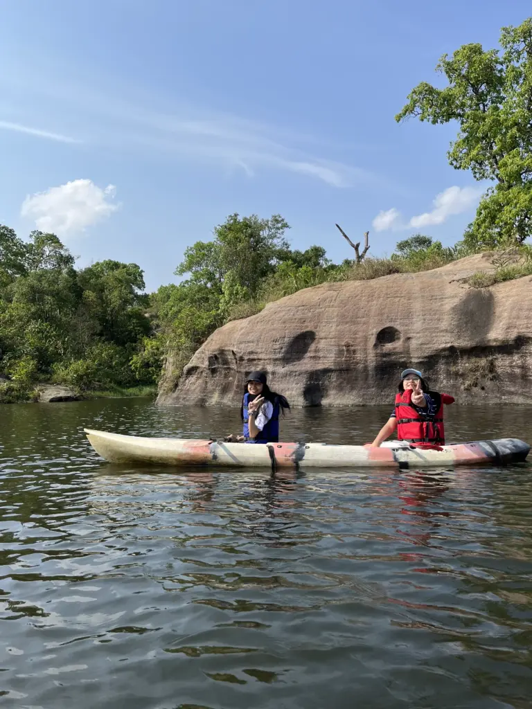 Two people kayaking on a calm lake surrounded by rocky cliffs at Mawlyngbna, Meghalaya