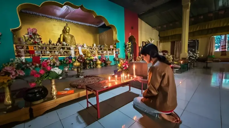 Woman lighting candles in front of a Buddha statue at Namphake Monastery, Assam