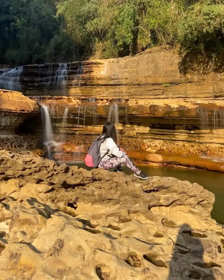 Woman sitting on rocks near cascading streams at Nohkalikai Falls Meghalaya