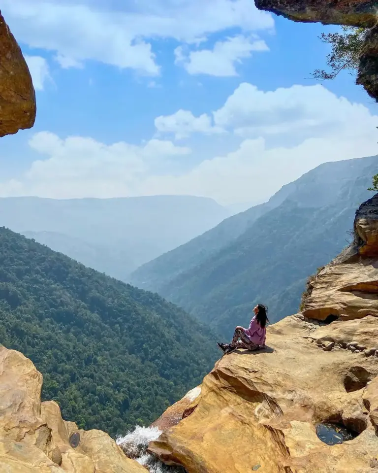 Woman sitting on rocky edge with mountain view at Nohkalikai Falls Meghalaya