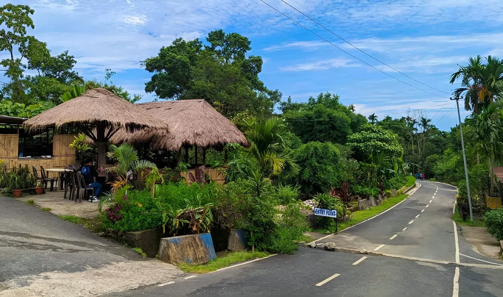 A scenic view of a roadside cafe with thatched roofs and lush greenery in Mawlynnong, Meghalaya