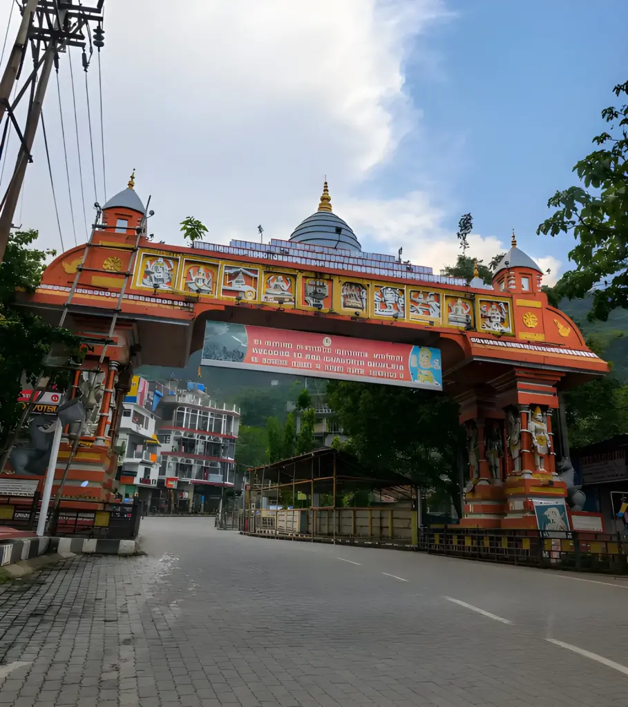 Entrance arch of Kamakhya Temple in Guwahati, Assam, with the temple dome rising behind it under a dramatic blue sky and