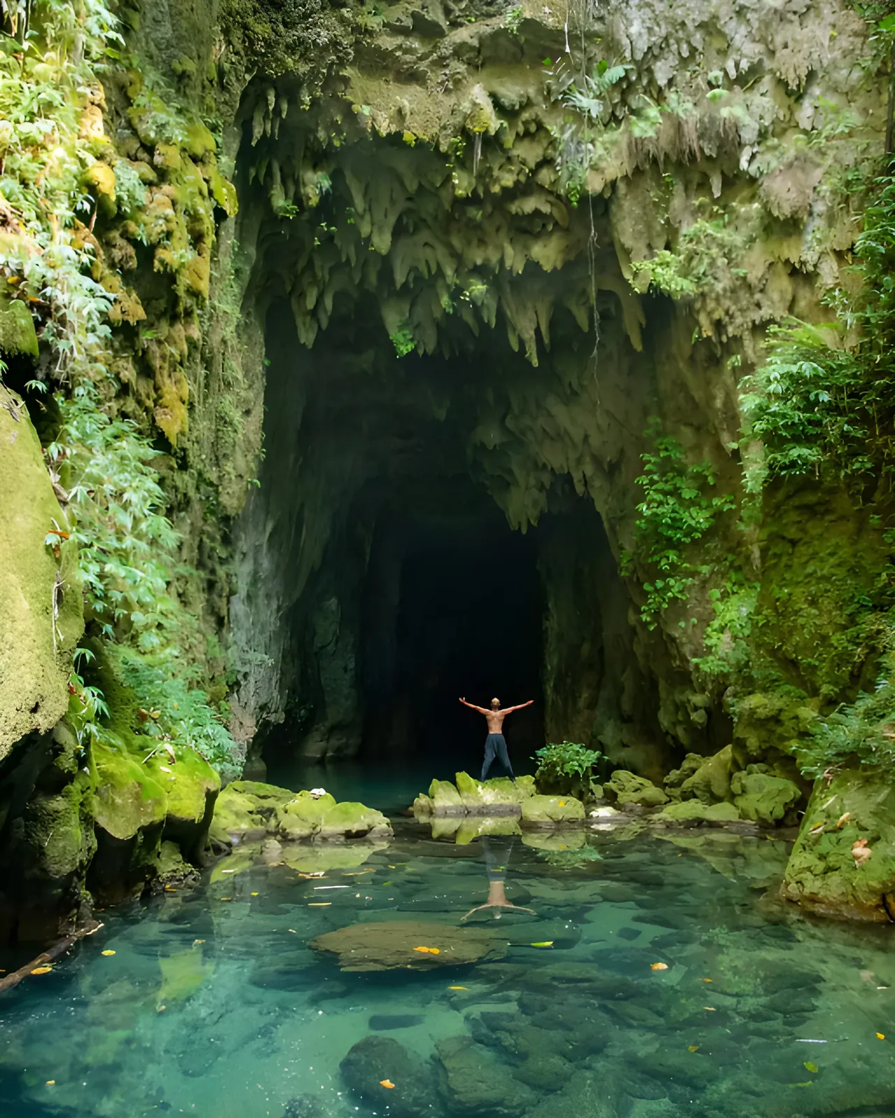Person standing at the entrance of Krem Cympe Cave beside a crystal-clear pool