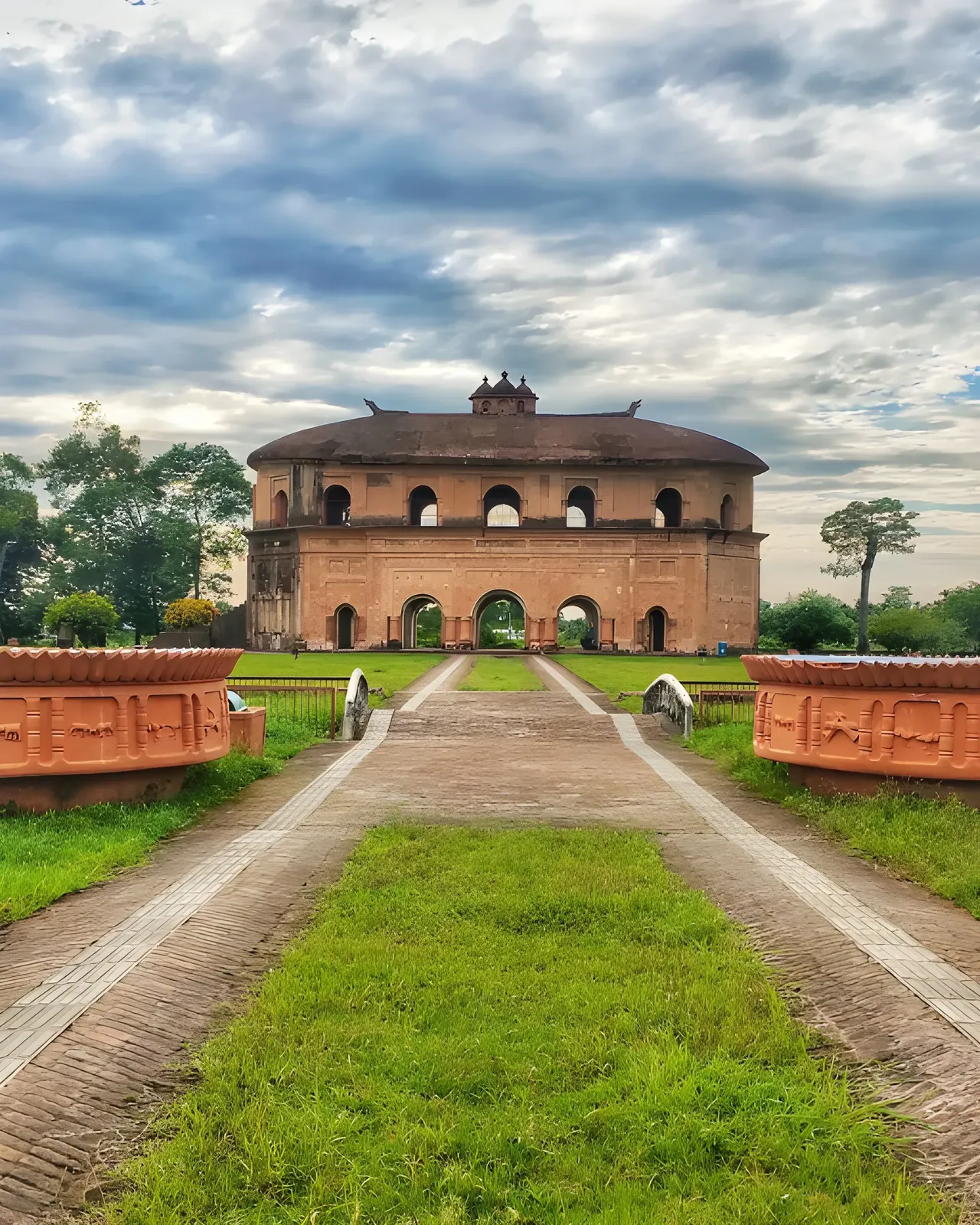 Rang Ghar, Sivasagar, framed by lush greenery beneath a cloudy sky