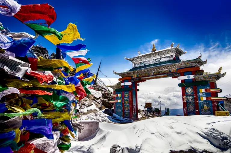 Colorful prayer flags flutter near the snow-covered gate at Sela Pass, Arunachal Pradesh.
