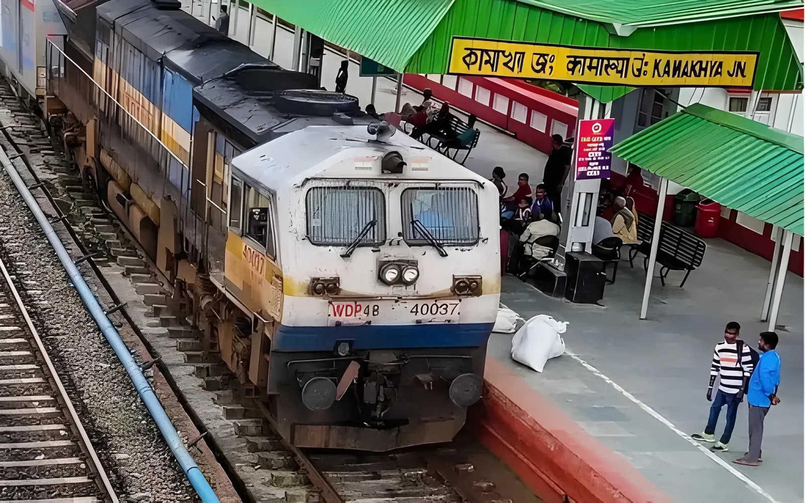 Train at Kamakhya Junction station with green hills and a rainbow in the background, Assam